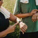 Two people checking their fitness watches while taking a break from a workout outside.