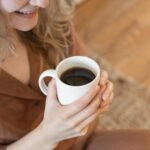 A woman in cozy clothing enjoys a warm cup of black coffee indoors.