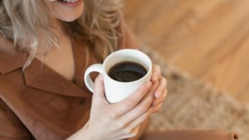 A woman in cozy clothing enjoys a warm cup of black coffee indoors.