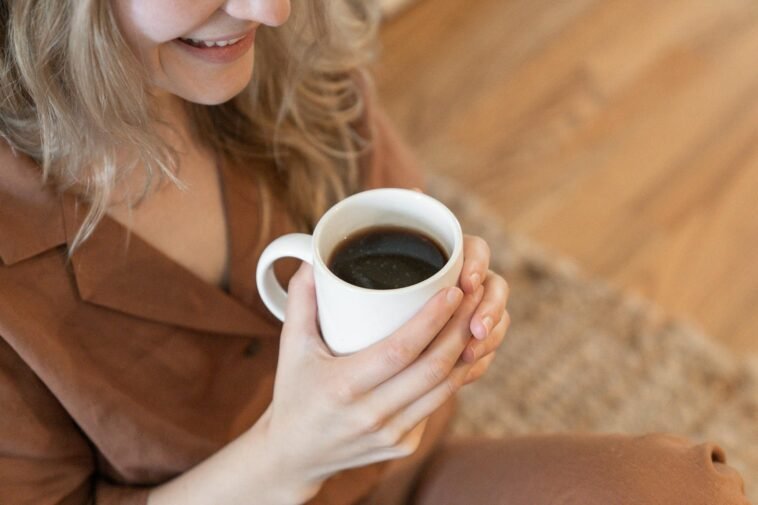 A woman in cozy clothing enjoys a warm cup of black coffee indoors.
