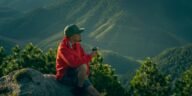 Man enjoys a serene moment in mountain scenery, sipping a drink at sunrise.