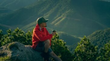 Man enjoys a serene moment in mountain scenery, sipping a drink at sunrise.
