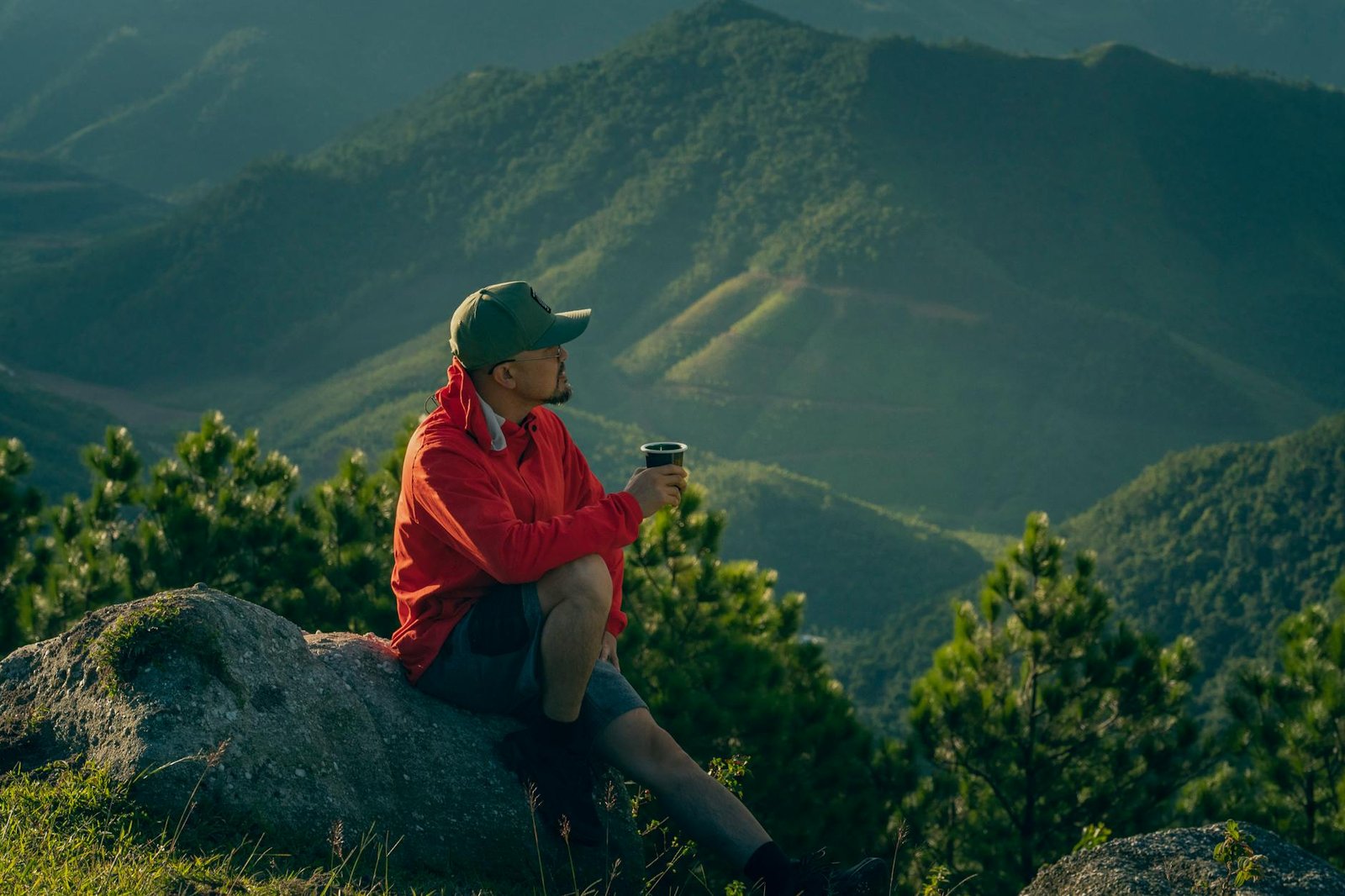 Man enjoys a serene moment in mountain scenery, sipping a drink at sunrise.