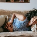 Young African American female with closed eyes lying on sofa while having acute stomach ache