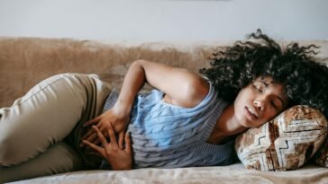 Young African American female with closed eyes lying on sofa while having acute stomach ache