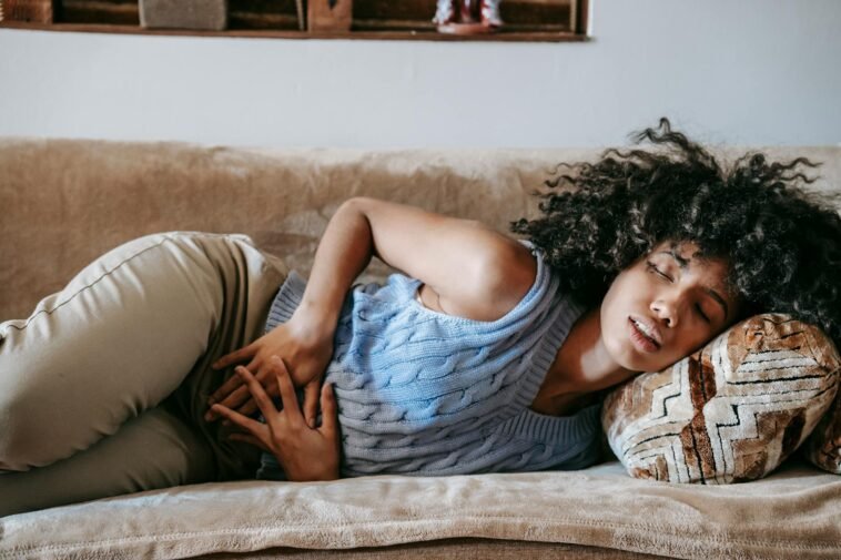 Young African American female with closed eyes lying on sofa while having acute stomach ache