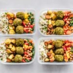 Colorful meal prep containers with falafel, chickpeas, rice, and vegetables for a healthy lifestyle.
