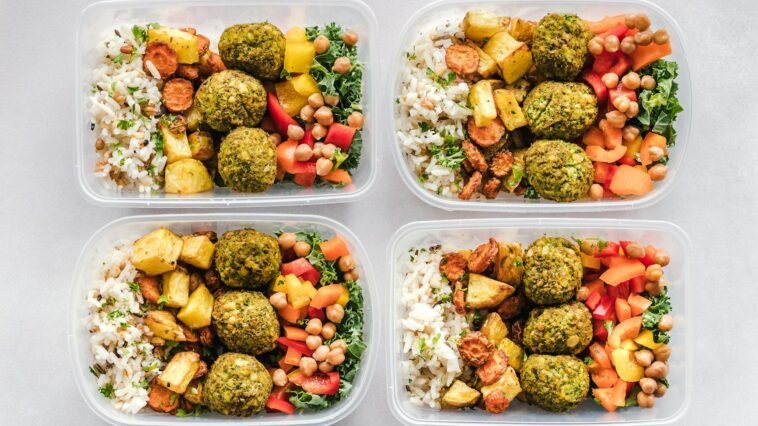 Colorful meal prep containers with falafel, chickpeas, rice, and vegetables for a healthy lifestyle.