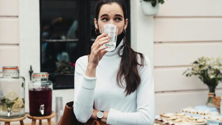 Casual outdoor scene of a woman drinking water at a social gathering, showcasing hydration.