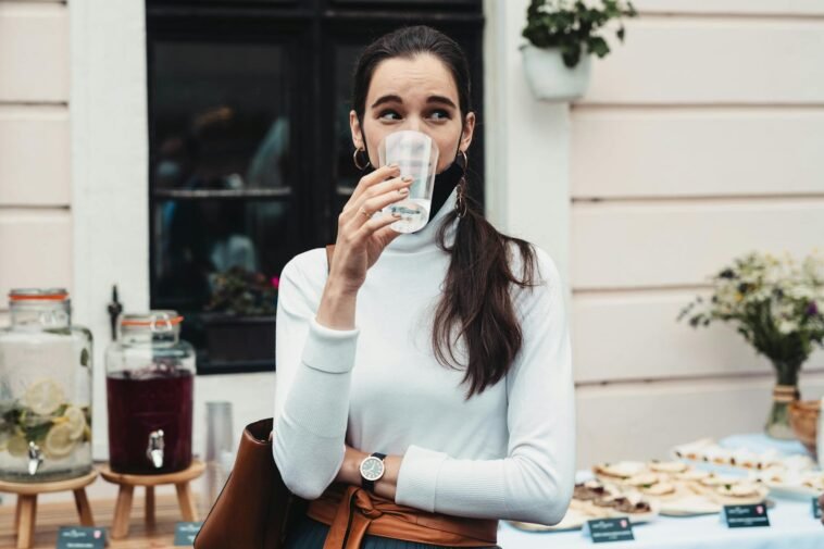 Casual outdoor scene of a woman drinking water at a social gathering, showcasing hydration.