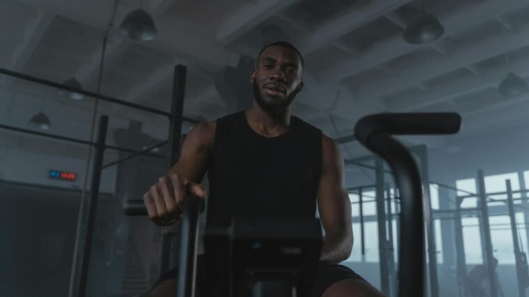 Black man training on exercise bike in modern gym setting, promoting fitness and healthy lifestyle.