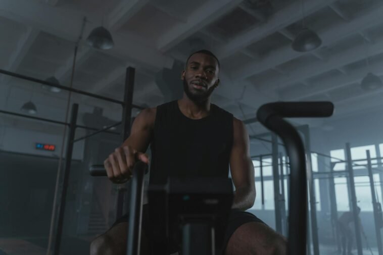Black man training on exercise bike in modern gym setting, promoting fitness and healthy lifestyle.