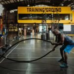 Athletic man engaging in a battle rope workout inside a modern gym setting for fitness training.