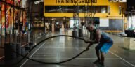 Athletic man engaging in a battle rope workout inside a modern gym setting for fitness training.