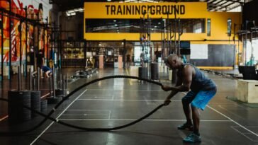 Athletic man engaging in a battle rope workout inside a modern gym setting for fitness training.