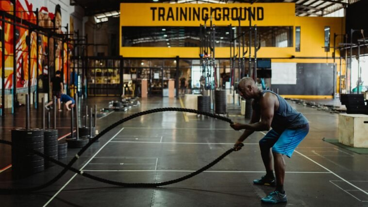 Athletic man engaging in a battle rope workout inside a modern gym setting for fitness training.