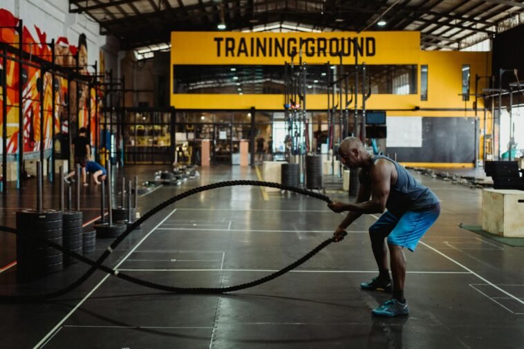 Athletic man engaging in a battle rope workout inside a modern gym setting for fitness training.