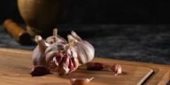 Close-up of garlic bulbs and cloves on a wooden cutting board with a rustic mortar in the background.