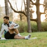 A young man stretches on the grass in a sunlit park, promoting fitness and relaxation.