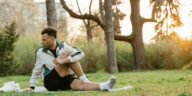 A young man stretches on the grass in a sunlit park, promoting fitness and relaxation.