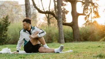 A young man stretches on the grass in a sunlit park, promoting fitness and relaxation.