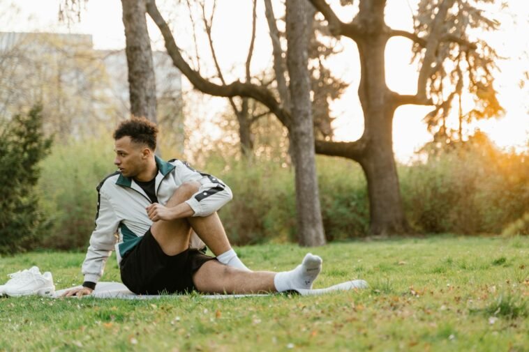 A young man stretches on the grass in a sunlit park, promoting fitness and relaxation.