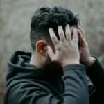 A man stands outdoors with his hands on his head, conveying stress and contemplation.