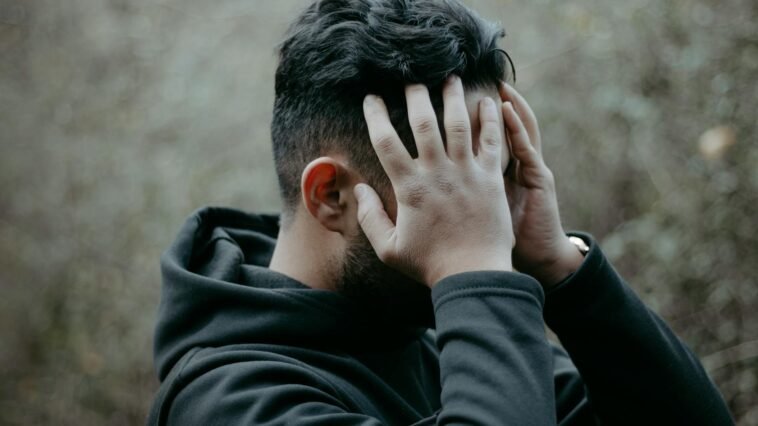 A man stands outdoors with his hands on his head, conveying stress and contemplation.
