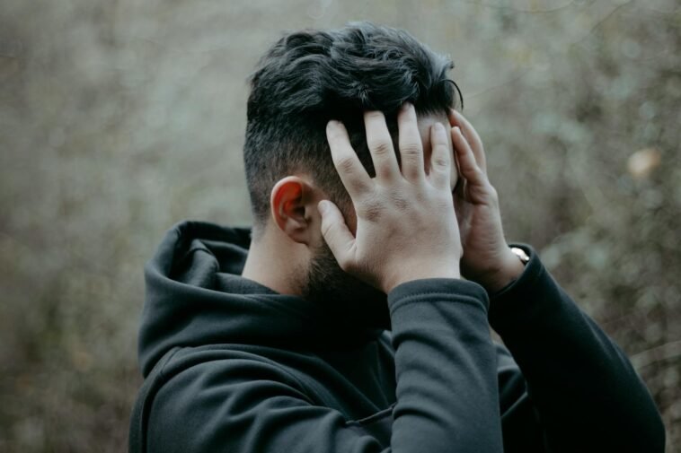 A man stands outdoors with his hands on his head, conveying stress and contemplation.