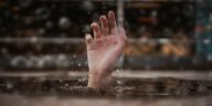 A single hand emerges from water, symbolizing a cry for help amidst a rainy setting.