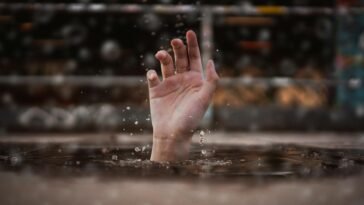 A single hand emerges from water, symbolizing a cry for help amidst a rainy setting.