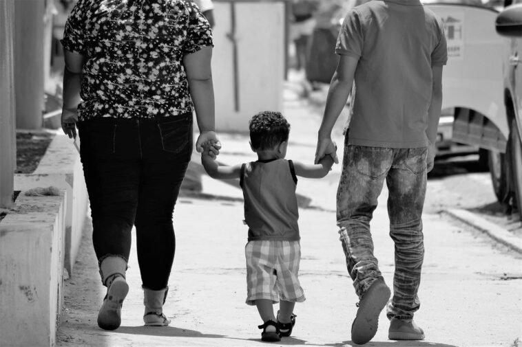 A family of three walks hand-in-hand on a sunny day in Santiago, Dominican Republic.
