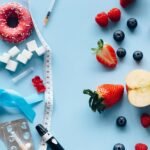 Flatlay of fruits, sugary treats, and diabetes tools on a blue background, symbolizing health choices.