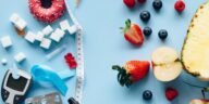 Flatlay of fruits, sugary treats, and diabetes tools on a blue background, symbolizing health choices.