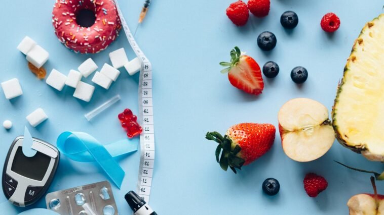 Flatlay of fruits, sugary treats, and diabetes tools on a blue background, symbolizing health choices.