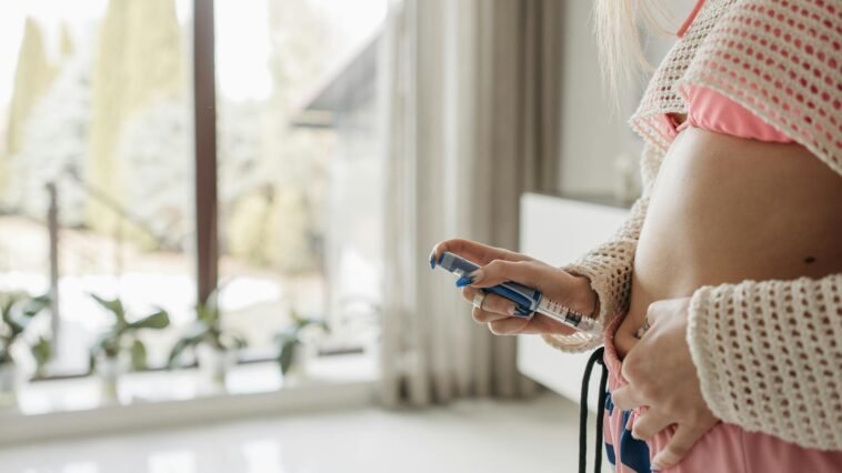 Focused woman administering insulin with pen in a home setting, emphasizing health care and diabetes management.