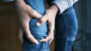 Close-up image of hands holding a knee in jeans, indicating pain or injury.
