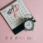 Calendar with pink ribbon, an alarm clock, and the text "Check breasts" signifies Breast Cancer Awareness.