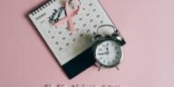 Calendar with pink ribbon, an alarm clock, and the text "Check breasts" signifies Breast Cancer Awareness.