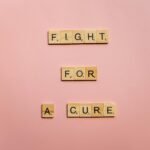 Wooden letter tiles on a pink background spell 'Fight for a Cure'. Motivational design.
