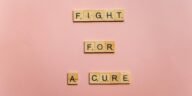 Wooden letter tiles on a pink background spell 'Fight for a Cure'. Motivational design.