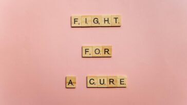 Wooden letter tiles on a pink background spell 'Fight for a Cure'. Motivational design.