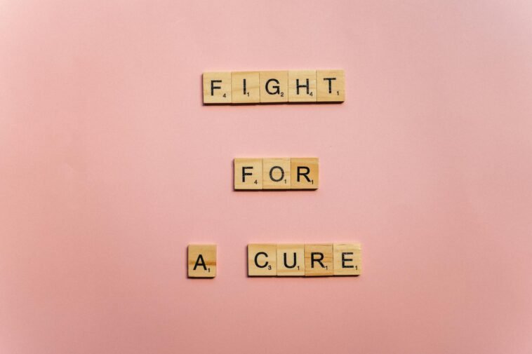 Wooden letter tiles on a pink background spell 'Fight for a Cure'. Motivational design.