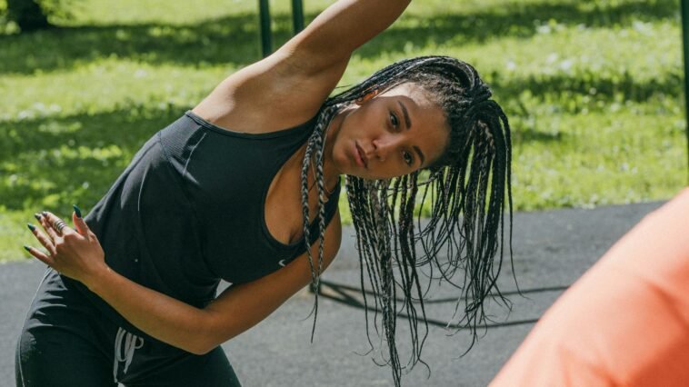 Young woman stretching in a sunny park for a fitness routine, promoting a healthy lifestyle.