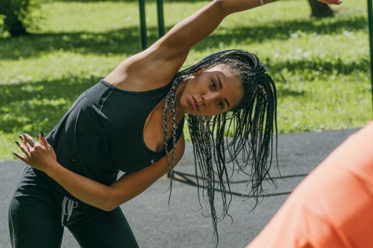Young woman stretching in a sunny park for a fitness routine, promoting a healthy lifestyle.
