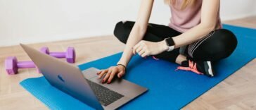 Woman in activewear using a laptop on a yoga mat with dumbbells, representing a healthy lifestyle.