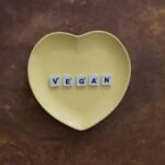 Yellow heart plate with letters spelling 'VEGAN' on a brown textured background.