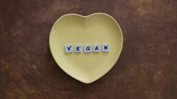 Yellow heart plate with letters spelling 'VEGAN' on a brown textured background.