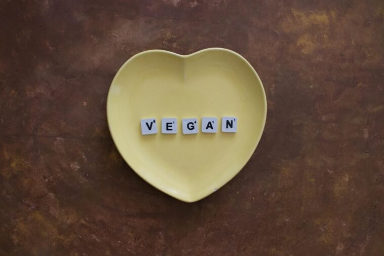 Yellow heart plate with letters spelling 'VEGAN' on a brown textured background.