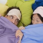 An interracial couple wearing sleep masks lying down on colorful pillows, portraying relaxation and rest.